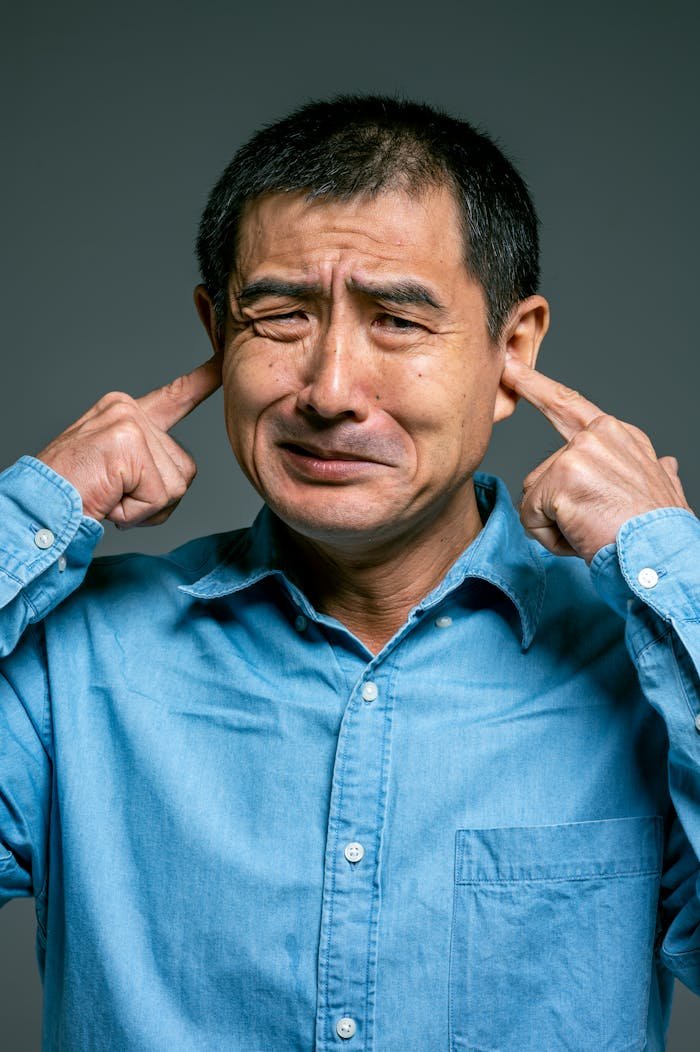 Close-up of a man covering his ears, expressing confusion and frustration.
